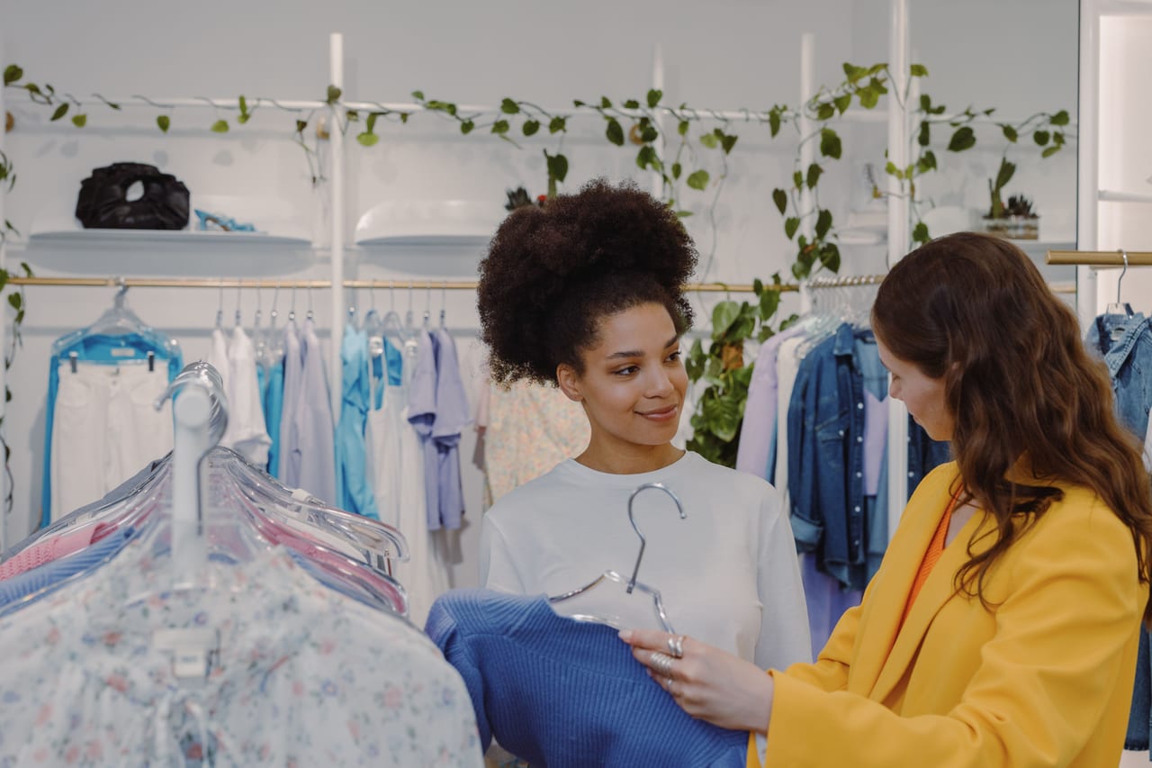 A customer browsing the rail in a fashion boutique with a stylist helping