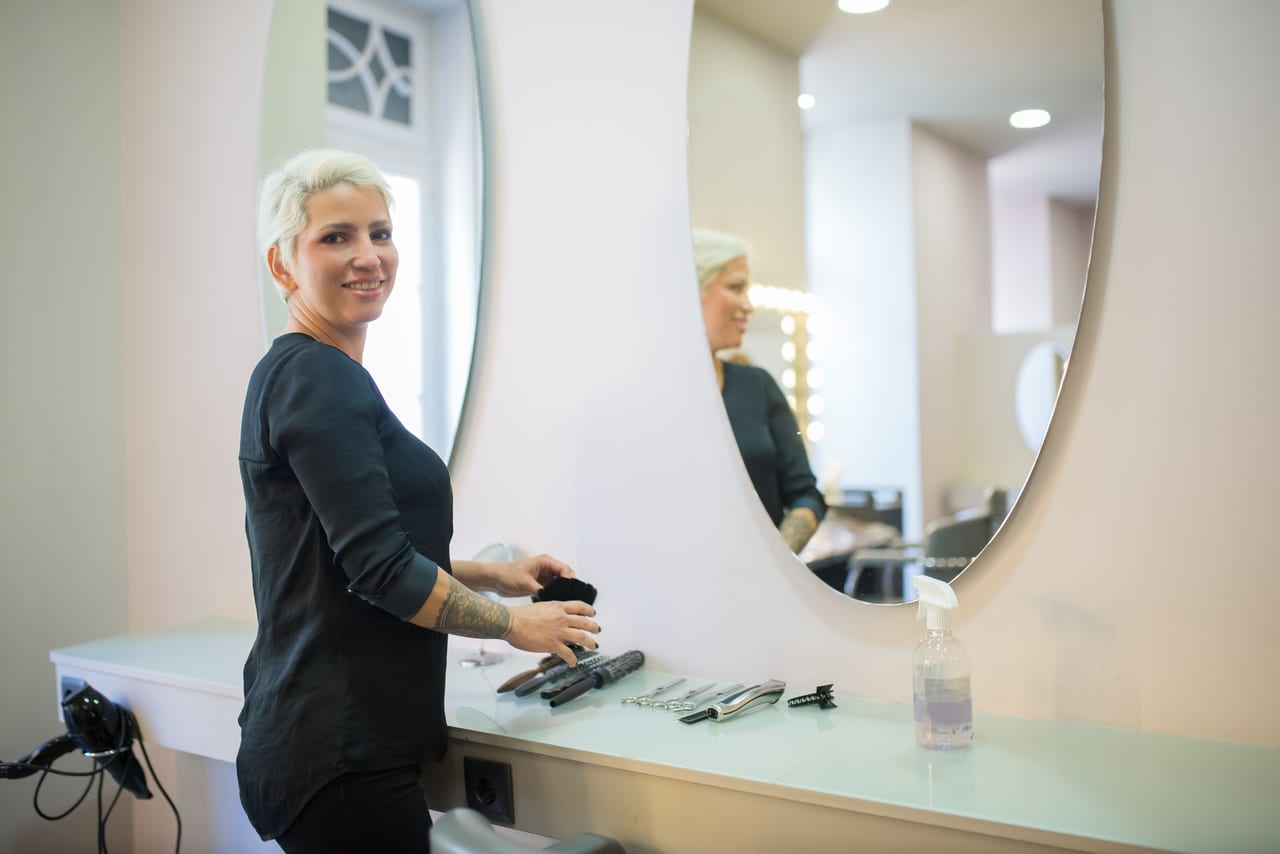 A stylist blow-drying a client at a mirror station